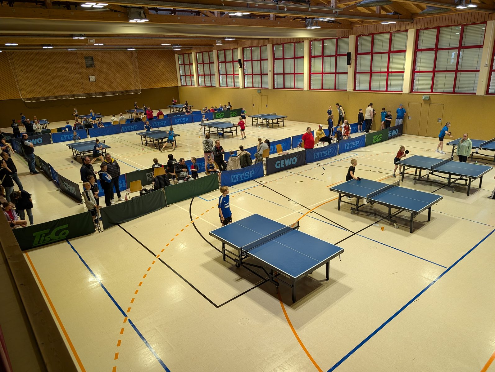Turnierhalle mit vielen Tischtennisplatten und Zuschauern bei einem Bezirksturnier.